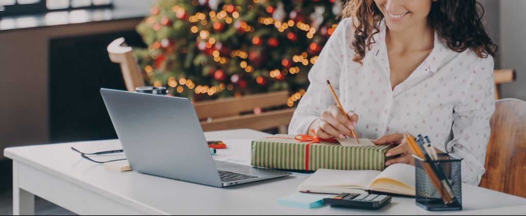 Pleased european woman office worker writing christmas letter, greeting card with holiday wishes